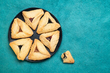Hamantaschen Pastry With Apricot, Raspberry And Prune Filling On A Black Ceramic Plate Against Handmade Bark Paper, A Traditional Pastry In Ashkenazi Jewish Cuisine For Holiday Of Purim