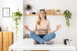 © Xavier Lorenzo - Smiling young businesswoman in lotus pose sitting on desk at home office. Happy female entrepreneur with closed eyes meditating taking a break for mental balance