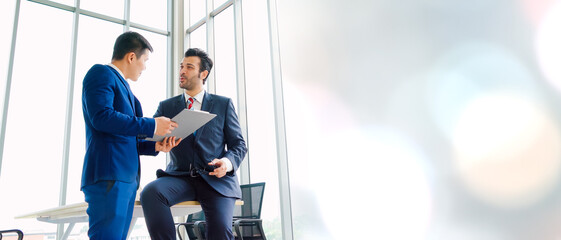 Two business people talk project strategy at office in widen view meeting room. Businessman discuss project planning with colleague at modern workplace .