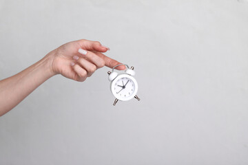 Wall Mural - Woman's hand holding an alarm clock on gray background