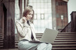 © splitov27 - Modern business lady sitting on the stairs with laptop near the business center. Freelance, Remote Work, Lifestyle