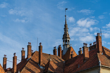 Wall Mural - Detail of a old building with a big tower with vane on the roof on a sunny day on a blue sky background. West Ukraine