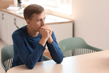 Wall Mural - Stressed young man sitting at table in kitchen