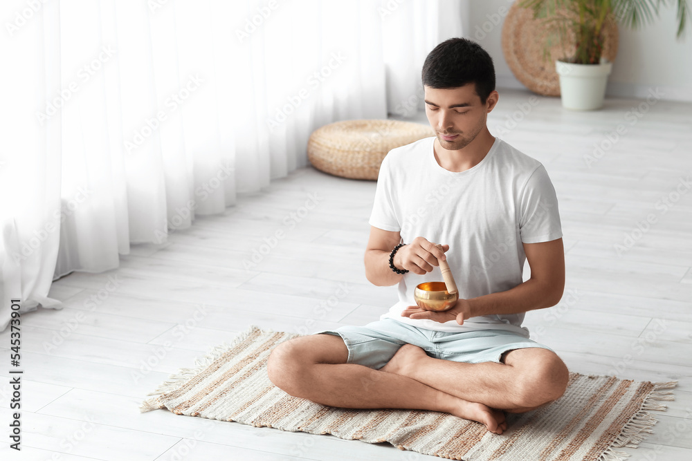 Young man with Tibetan singing bowl meditating at home