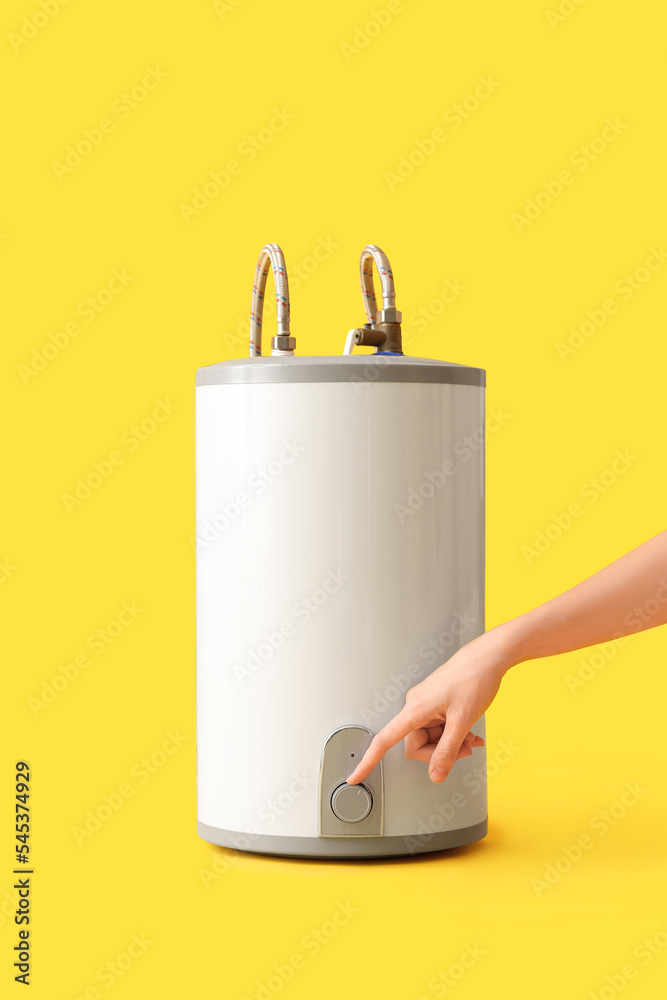 Woman adjusting electric boiler on yellow background