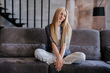 Attractive Blonde Caucasian Girl In Casual Sitting On Cozy Sofa At Home, Bored Waiting For Husband Being In Cute Mood. Beautiful Swedish Young Woman Tired, Relaxing After Work At Comfortable Penthouse