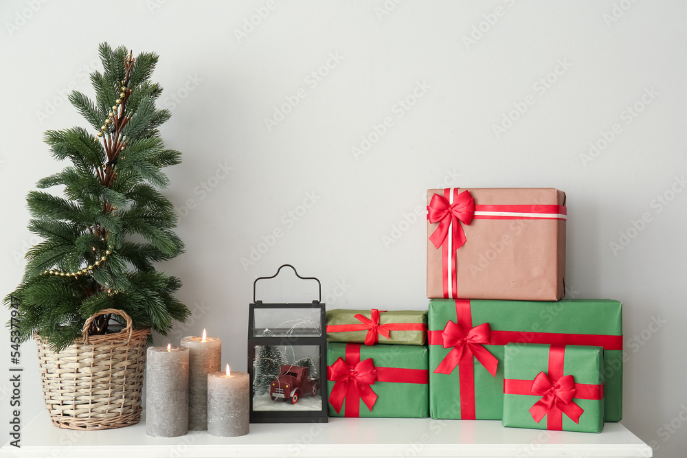 Christmas tree with presents and candles on mantelpiece near light wall