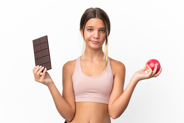 Wall Mural - Little caucasian girl isolated on white background having doubts while taking a chocolate tablet in one hand and an apple in the other