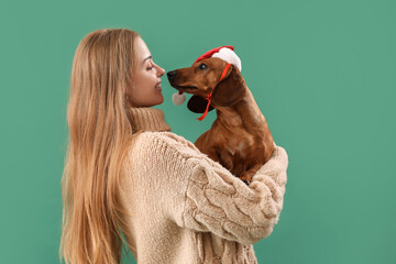 Wall Mural - Young woman with dachshund dog in Santa hat on green background