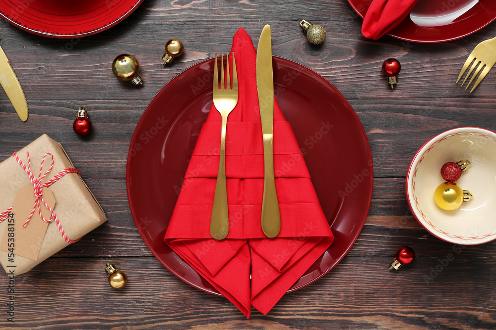 Beautiful table setting with Christmas balls and gift on wooden background