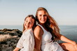 Sea family vacation together, happy mom and teenage daughter hugging and smiling together over sunset sea view. Beautiful woman with long hair relaxing with her child. Concept of happy friendly family