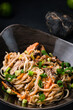 Asian food udon noodles with teriyaki beef and vegetables: red pepper, tomatoes, onion and sesame seeds, closeup.