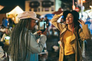 African mother and daughter having fun using vintage old video camera outdoor - Focus on senior woman hat