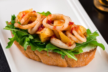 Wall Mural - Italian food bruschetta with fried squid, arugula, cream cheese and sauce, closeup.