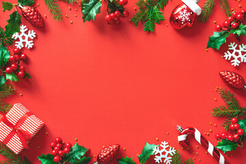 Wall Mural - christmas tree branches, holly berries and decorations on red background with space for text