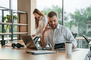 Boss is talking by phone. Man and woman are working in the modern office together