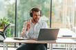 © standret - Laptop, headphones, positive look. Man in formal clothes is working in the modern office