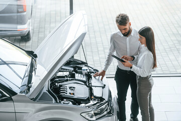 Wall Mural - What's under the hood. Man with woman in white clothes are in the car dealership together