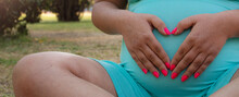 Mujer Embarazada Sosteniendo Su Panza Con Las Manos Formando Un Corazon, Al Atardecer En El Parque