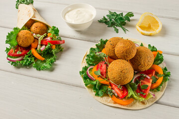 Wall Mural - Tortillas, wrapped falafel balls, with fresh vegetables, vegetarian healthy food, on a wooden white background, no people, selective focus.