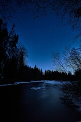 Sticker - Vertical shot of a calm river surrounded by snow in a vibrant blue sky background at night