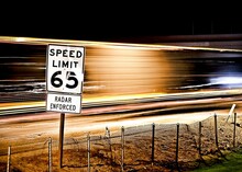 Pole With A Speed Limit 65 Sign On The Background Of Light Trails Of Cars In A Long Exposure Shot