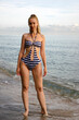 Young beautiful slender woman in a striped swimsuit stand at the seashore. Indonesia, Bali