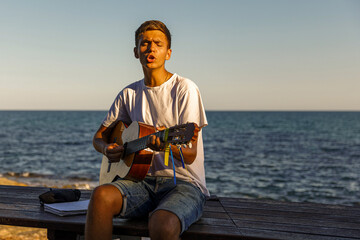 A young stylish guy plays the guitar on the embankment by the sea, the concept of music and relaxation