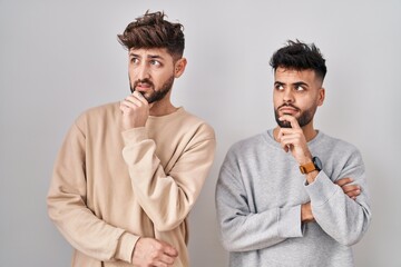 Wall Mural - Young homosexual couple standing over white background thinking worried about a question, concerned and nervous with hand on chin