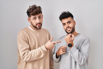 Wall Mural - Young homosexual couple standing over white background in hurry pointing to watch time, impatience, looking at the camera with relaxed expression