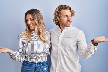 Sticker - Young couple standing over blue background smiling showing both hands open palms, presenting and advertising comparison and balance