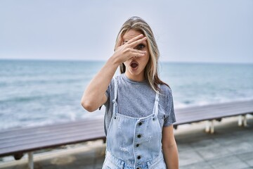 Wall Mural - Young caucasian woman outdoors peeking in shock covering face and eyes with hand, looking through fingers with embarrassed expression.