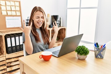 Canvas Print - Young brunette woman working at the office with laptop shouting with crazy expression doing rock symbol with hands up. music star. heavy concept.