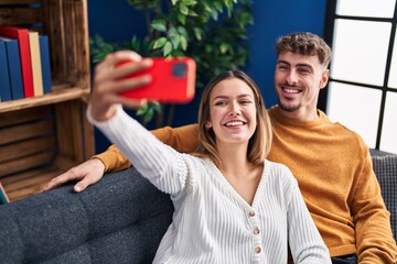 Poster - Young man and woman couple make selfie by the smartphone sitting on sofa at home