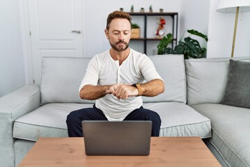 Wall Mural - Middle age man using laptop at home checking the time on wrist watch, relaxed and confident