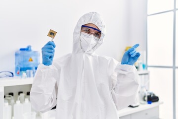 Poster - Young blonde woman holding cpu computer processor at laboratory smiling happy pointing with hand and finger to the side