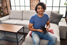 Young Hispanic Man Showing Empty Wallet Sitting On Sofa At Home