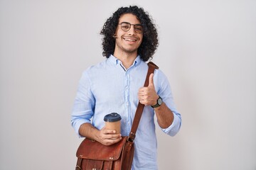 Canvas Print - Hispanic man with curly hair drinking a cup of take away coffee doing happy thumbs up gesture with hand. approving expression looking at the camera showing success.