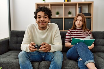 Poster - Man playing video game while unhappy girlfriend read book at home.