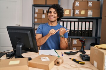 Poster - Hispanic man with curly hair working at small business ecommerce pointing to the back behind with hand and thumbs up, smiling confident