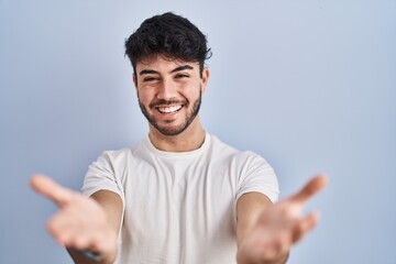 Sticker - Hispanic man with beard standing over white background smiling cheerful offering hands giving assistance and acceptance.