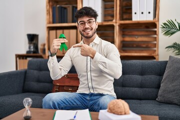 Sticker - Hispanic man with beard holding support green ribbon at therapy clinic smiling happy pointing with hand and finger