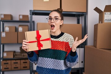 Poster - Young hispanic girl working at small business ecommerce holding box celebrating victory with happy smile and winner expression with raised hands