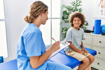 Poster - Mother and son wearing physiotherapist uniform having rehab session writing on clipboard at physiotherapy clinic