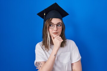 Poster - Blonde caucasian woman wearing graduation cap looking confident at the camera smiling with crossed arms and hand raised on chin. thinking positive.