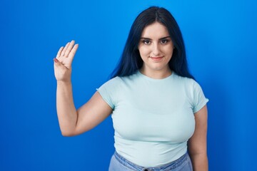 Canvas Print - Young modern girl with blue hair standing over blue background showing and pointing up with fingers number four while smiling confident and happy.