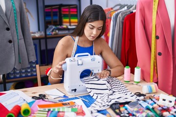 Canvas Print - Young beautiful hispanic woman tailor using sewing machine at tailor shop