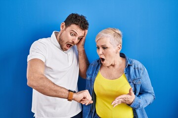 Canvas Print - Young brazilian mother and son standing over blue background looking at the watch time worried, afraid of getting late