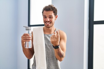 Sticker - Young hispanic man wearing sportswear drinking water beckoning come here gesture with hand inviting welcoming happy and smiling