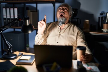 Canvas Print - Middle age man with grey hair working at the office at night amazed and surprised looking up and pointing with fingers and raised arms.